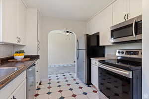 Kitchen with stainless steel appliances, white cabinetry, arched walkways, and ceiling fan