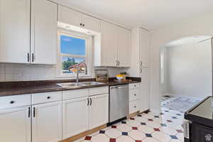 Kitchen with black electric range, arched walkways, dark countertops, and white cabinetry