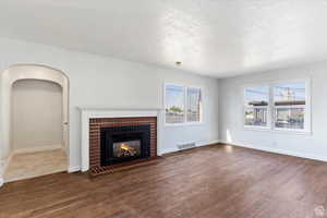 Unfurnished living room featuring a fireplace, dark wood finished floors, and a textured ceiling