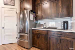 Kitchen featuring light countertops, freestanding refrigerator, dark wood finish cabinets, tasteful backsplash, and light wood-type flooring