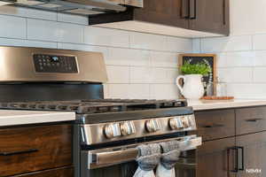 Kitchen view of dark wood finish cabinetry, stainless steel range with gas cooktop, tasteful backsplash, and light countertops