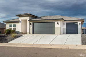 Prairie-style house with an attached garage, stucco siding, concrete driveway, and a tile roof