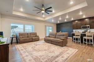 Living room featuring ceiling fan, light wood-style flooring, a tray ceiling, recessed lighting, and an accent wall