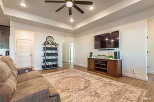 Living area featuring a ceiling fan, a tray ceiling, light wood-type flooring, and recessed lighting