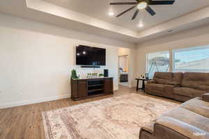 Living area with ceiling fan, light wood-style flooring, a tray ceiling, and recessed lighting