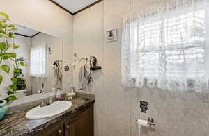 Half bath with vanity, wallpapered walls, and crown molding