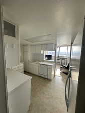 Kitchen with light countertops, freestanding refrigerator, white cabinets, dishwasher, and a textured ceiling