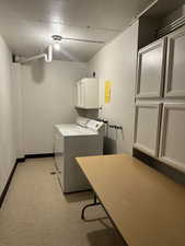 Laundry area just outside condo with cabinet space, independent washer and dryer, and a textured ceiling