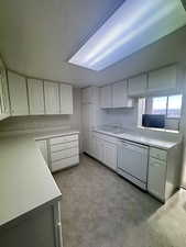 Kitchen with light countertops, white cabinets, white dishwasher, laminate flooring, and wallpapered walls
