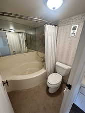 Bathroom featuring shower / bath combo with shower curtain, a textured ceiling, and wallpapered walls