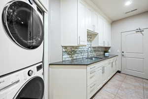 Laundry room featuring stacked washer / dryer, light tile patterned floors, and recessed lighting