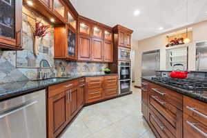 Kitchen with built in appliances, hanging light fixtures, dark stone counters, tasteful backsplash, and light tile patterned floors