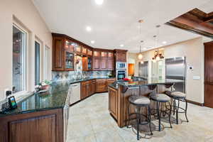Kitchen with glass fronted cabinets, a kitchen bar, dark stone counters, decorative light fixtures, and arched walkways