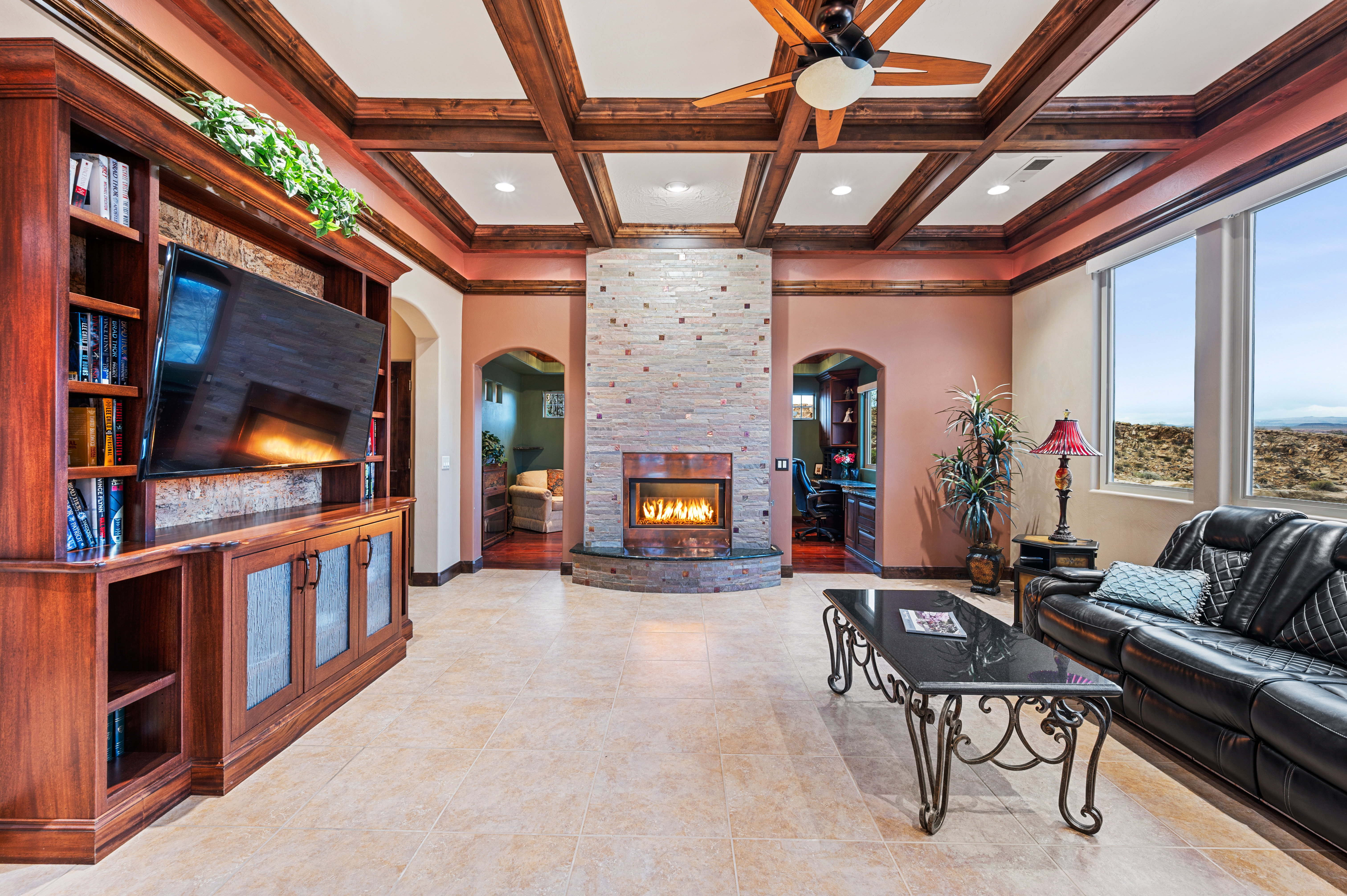 Living room featuring coffered ceiling, a stone fireplace, arched walkways, ceiling fan, and recessed lighting