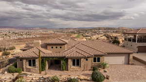 Mediterranean / spanish house featuring stone siding, a chimney, decorative driveway, and an attached garage