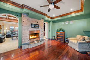 Living room featuring a raised ceiling, arched walkways, a ceiling fan, a fireplace, and recessed lighting