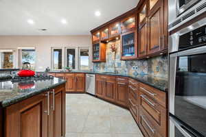 Kitchen featuring stainless steel appliances, dark stone counters, light tile patterned floors, recessed lighting, and glass insert cabinets