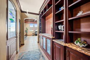 Hallway featuring light tile patterned flooring, arched walkways, ornamental molding, and inlaid floor details