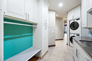 Laundry area with stacked washer and dryer, light tile patterned floors, and recessed lighting