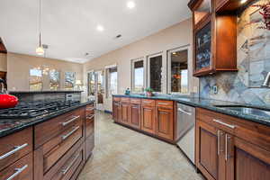 Kitchen with dark stone counters, tasteful backsplash, glass fronted cabinets, stainless steel dishwasher, and black gas cooktop