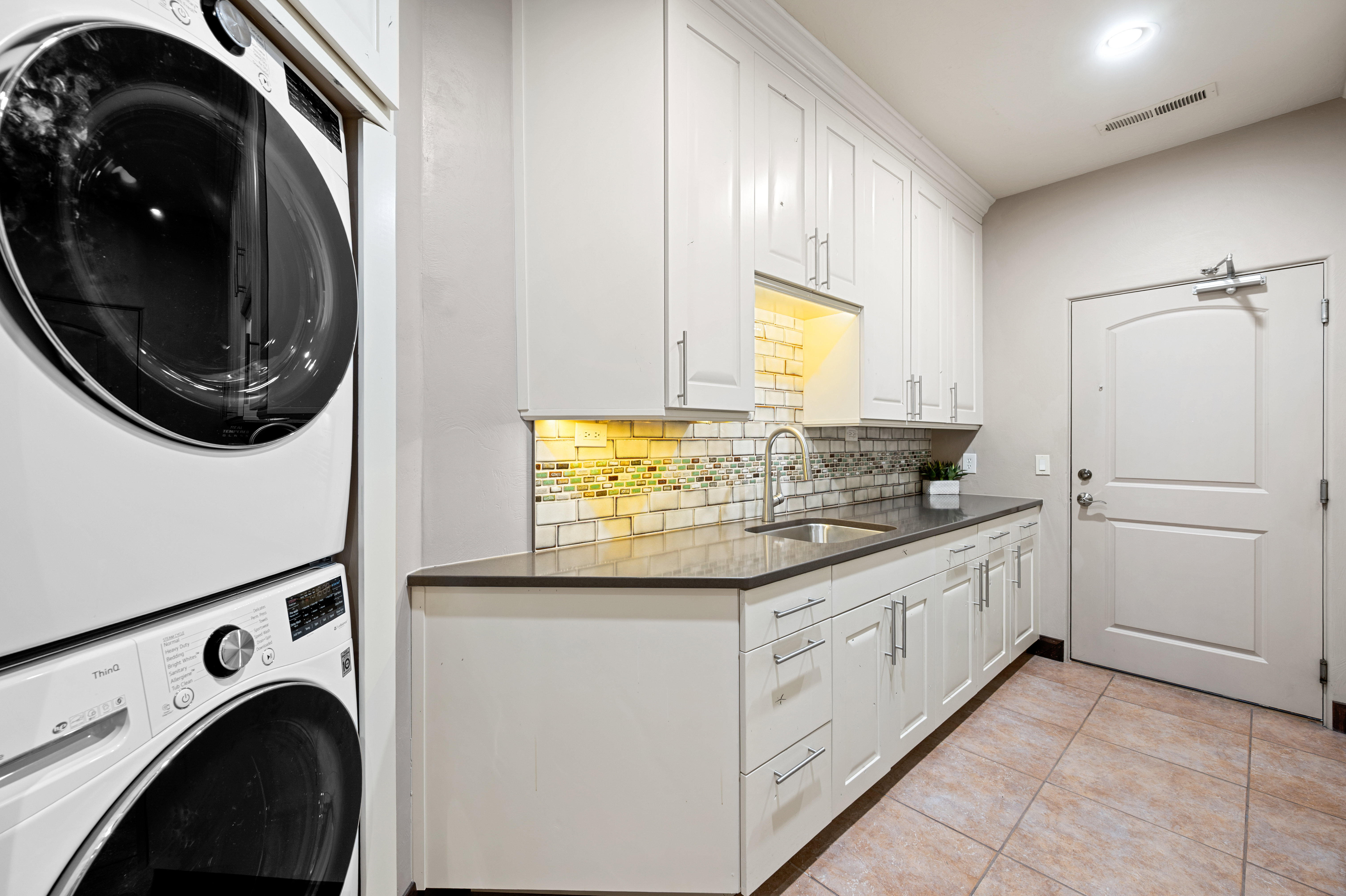 Laundry area with stacked washer and dryer and light tile patterned floors