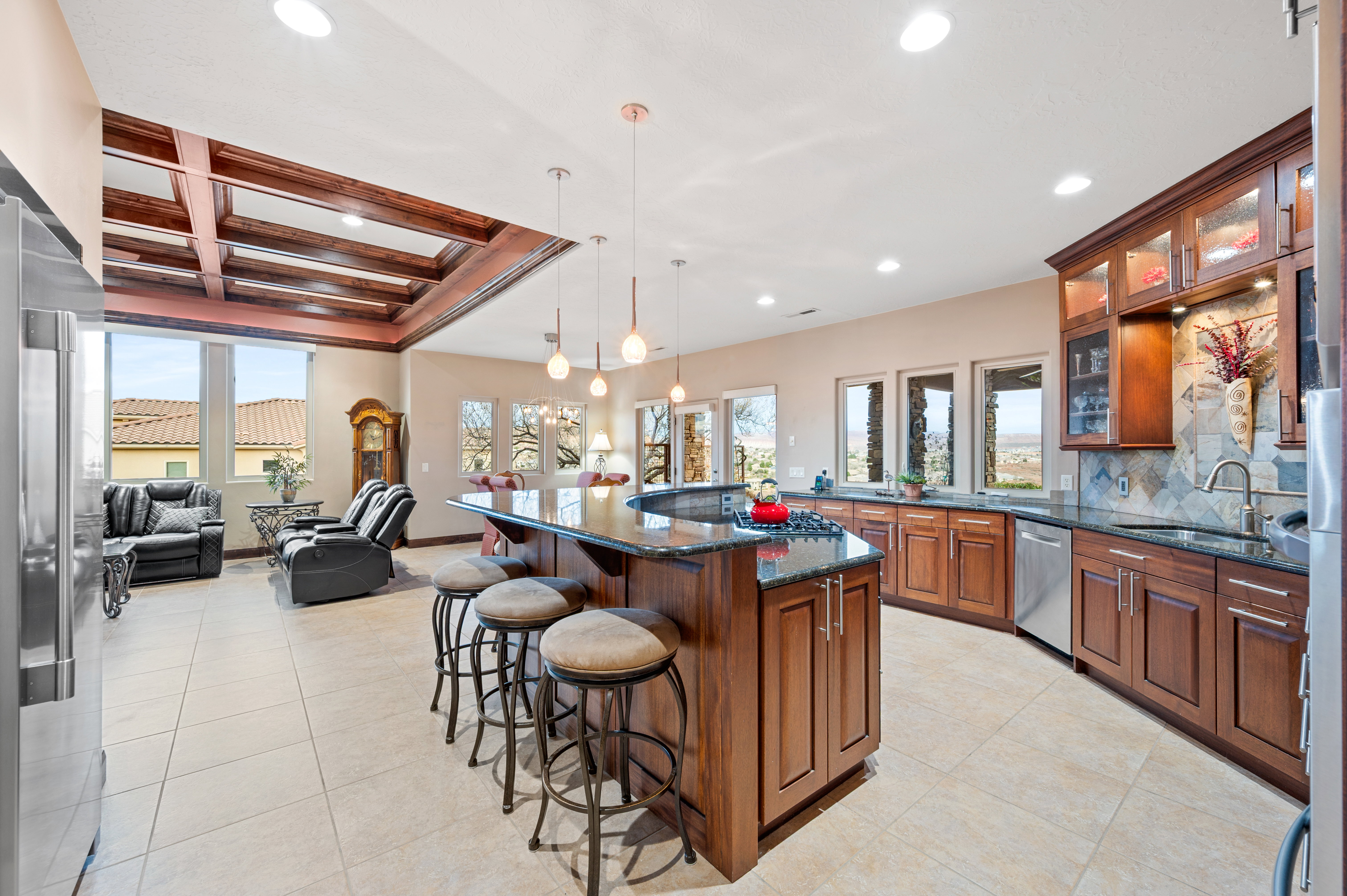 Kitchen featuring dark stone countertops, glass insert cabinets, a breakfast bar area, coffered ceiling, and wood finish cabinets