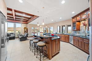 Kitchen featuring dark stone countertops, glass insert cabinets, a breakfast bar area, coffered ceiling, and wood finish cabinets