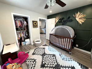 Bedroom with a decorative wall, wood finished floors, a walk in closet, a nursery area, and ceiling fan