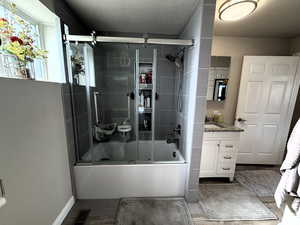 Full bath with vanity, shower / bath combination with glass door, and a textured ceiling