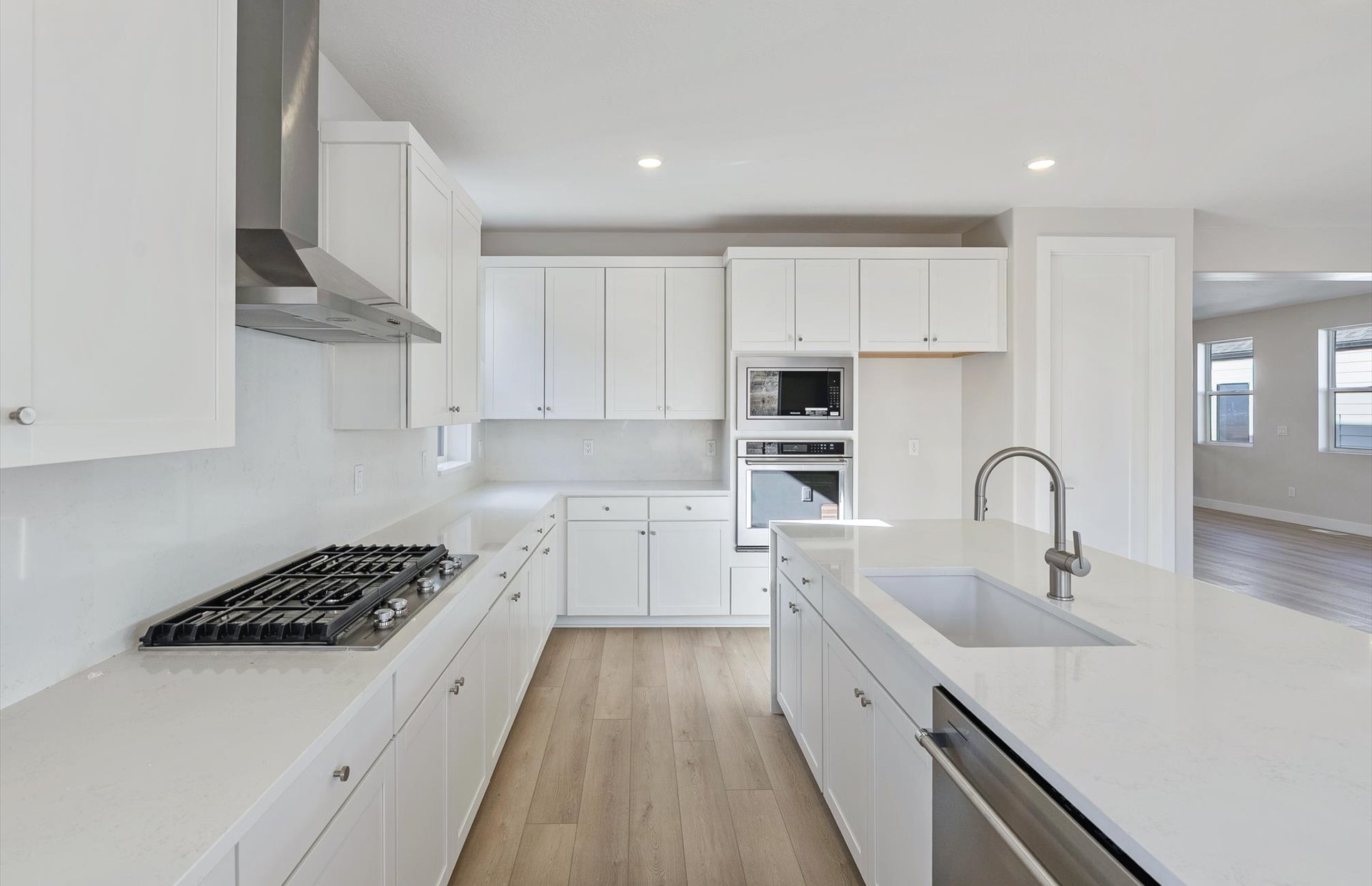 Kitchen with light wood-type flooring, white cabinets, stainless steel appliances, light stone counters, and recessed lighting