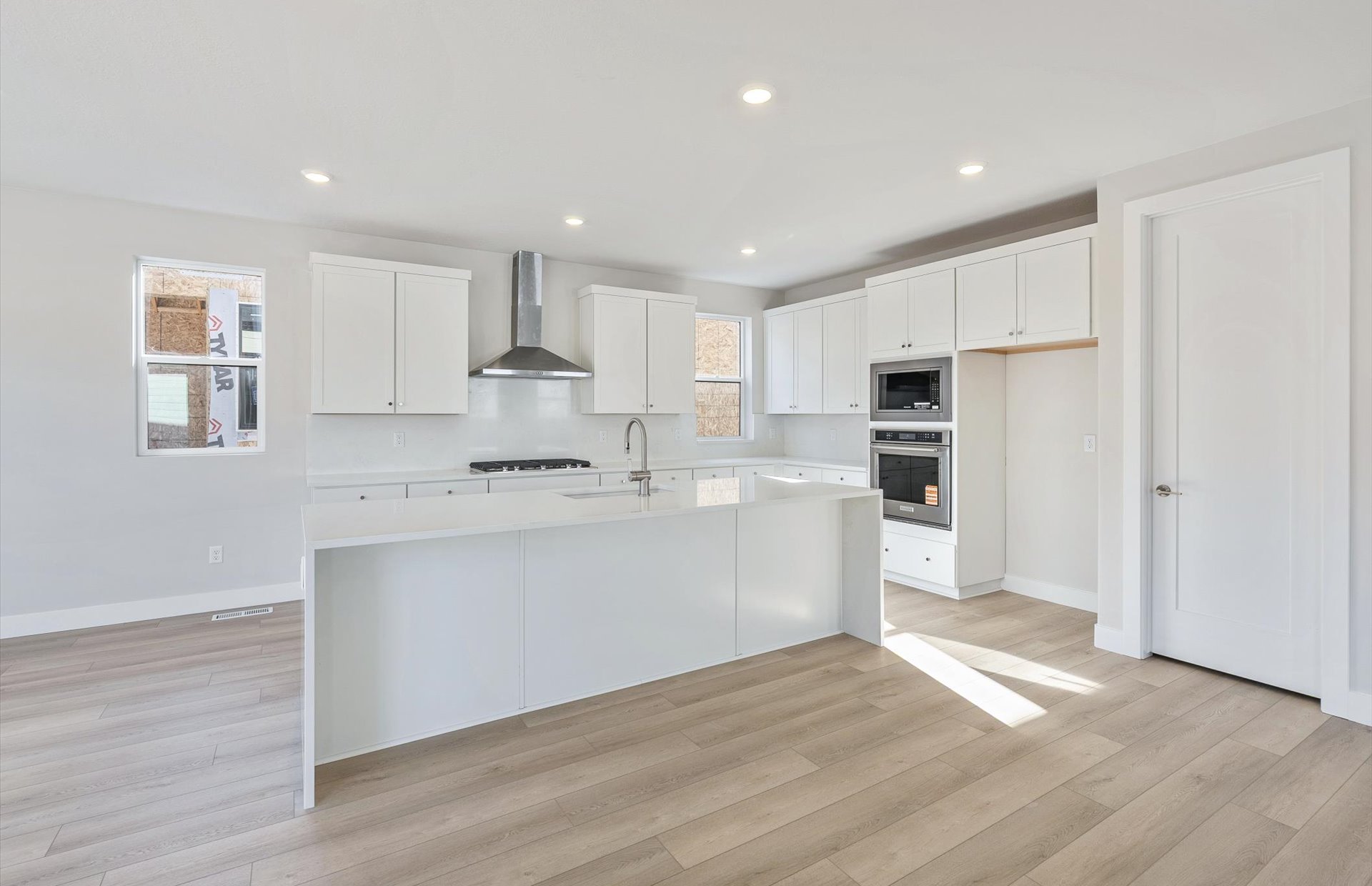 Kitchen featuring white cabinetry, a kitchen island with sink, stainless steel appliances, light wood-type flooring, and light stone counters