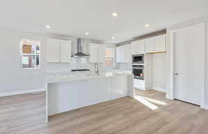 Kitchen featuring white cabinetry, a kitchen island with sink, stainless steel appliances, light wood-type flooring, and light stone counters