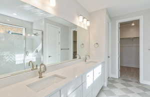 Bathroom with a spacious closet, double vanity, light floors, and a stall shower