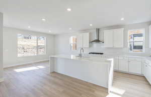 Kitchen featuring white cabinets, a kitchen island with sink, light stone counters, light wood finished floors, and recessed lighting