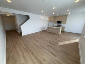 Kitchen with open floor plan, light wood-style flooring, light countertops, an island with sink, and stainless steel appliances