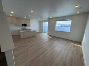 Kitchen featuring open floor plan, light wood finished floors, a center island with sink, light countertops, and light wood finish cabinetry