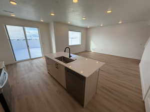 Kitchen with open floor plan, an island with sink, dishwashing machine, light wood finished floors, and range