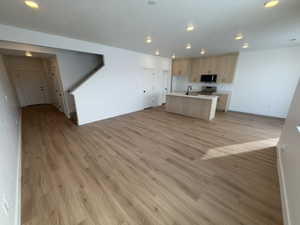 Kitchen featuring open floor plan, light wood-style flooring, light countertops, a center island with sink, and black microwave