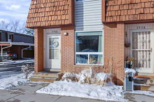 Snow covered property entrance featuring brick siding and mansard roof