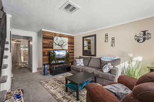 Carpeted living room with a textured ceiling, a ceiling fan, crown molding, and wood walls