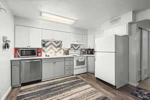 Kitchen featuring stainless steel appliances, light countertops, two tone color scheme, a textured ceiling, and dark wood-style floors