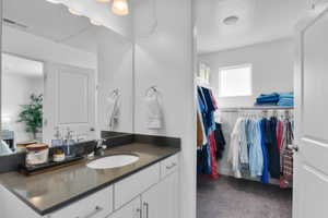 Bathroom with vanity, a walk in closet, and dark colored carpet