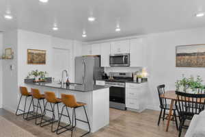 Kitchen with stainless steel appliances, a peninsula, a breakfast bar area, light wood-style flooring, and white cabinets
