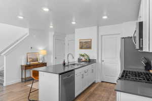 Kitchen with a peninsula, white cabinetry, stainless steel appliances, dark wood finished floors, and recessed lighting