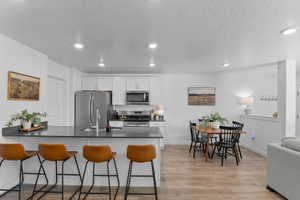 Kitchen featuring a peninsula, a breakfast bar area, stainless steel appliances, light wood finished floors, and white cabinets