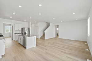 Kitchen with a center island with sink, light stone counters, white cabinets, light wood-style flooring, and stainless steel appliances