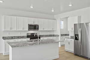 Kitchen featuring stainless steel appliances, light stone countertops, white cabinets, light wood finished floors, and recessed lighting