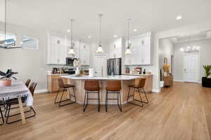 Dual tone kitchen with hanging lights, a breakfast bar area, backsplash, light wood-style floors, and an island with sink