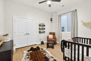 Bedroom featuring a crib, light wood-style floors, a closet, and ceiling fan