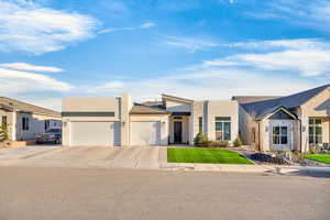 View of front of home featuring an attached garage, stone siding, stucco siding, driveway, and a front yard